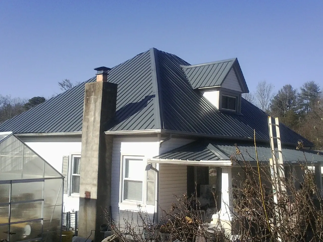 Dark blue standing seam metal roof on a white farmhouse with dormer — Slate & Tile Roof Repair by Roofing Brothers in Lenoir City