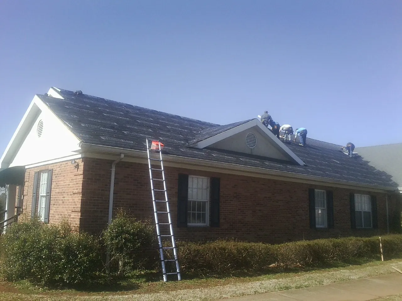 Crew tearing shingles off a brick ranch roof with a ladder set — Metal Roof Repair work by our crew in Lenoir City