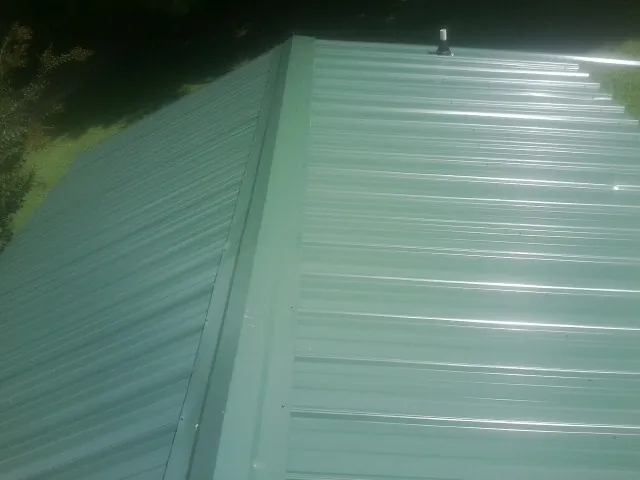 New green metal panels meeting at the ridge of a roof — Flat Roof Repair work by our crew in Lenoir City