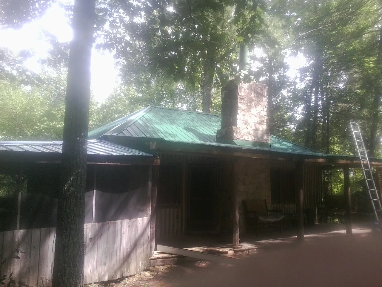 Green metal roof and stone chimney above a log cabin porch in Lenoir City