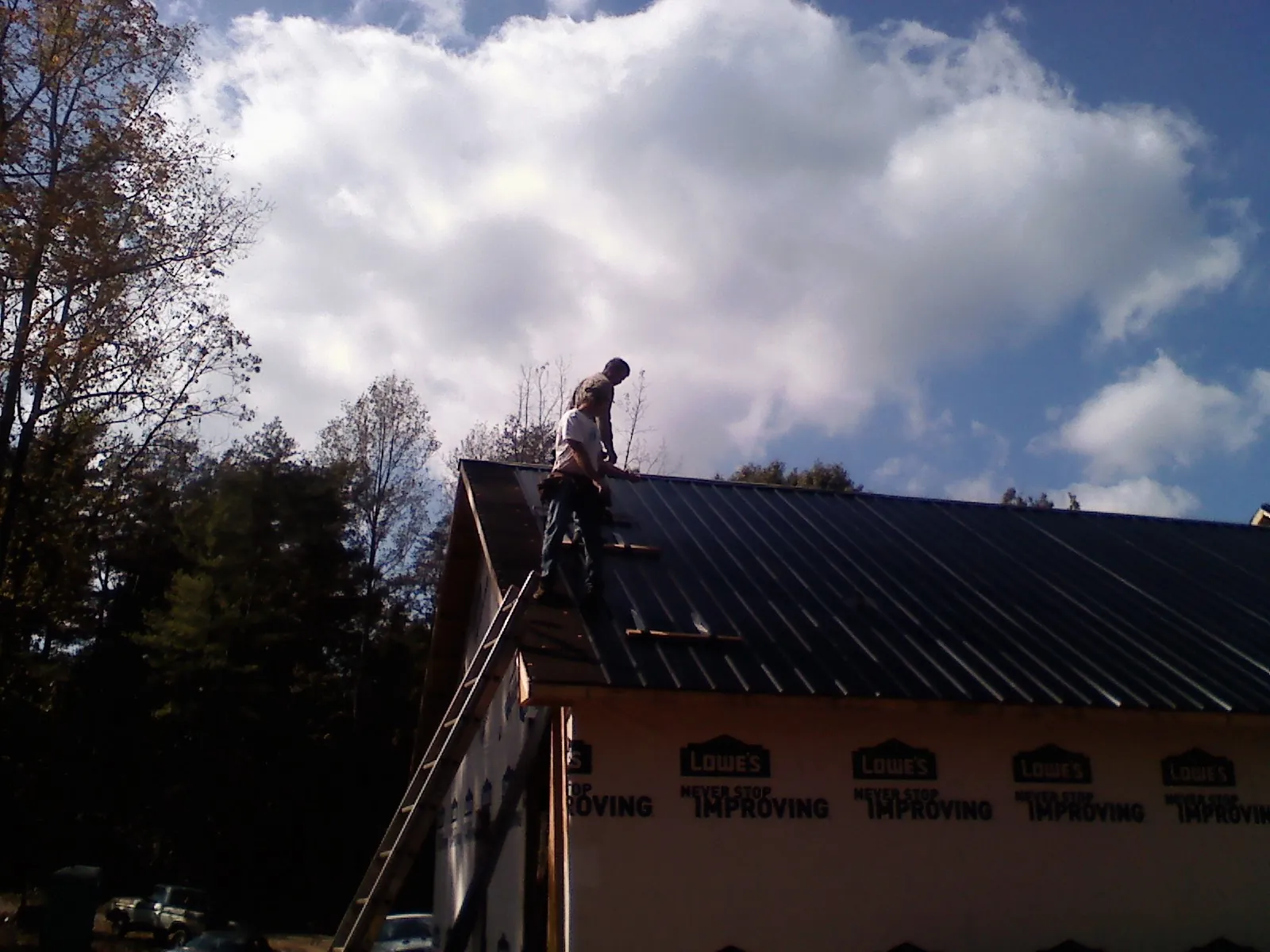 Roofer fastening dark metal panels high against a cloudy sky, from a Roof Inspection job in Lenoir City