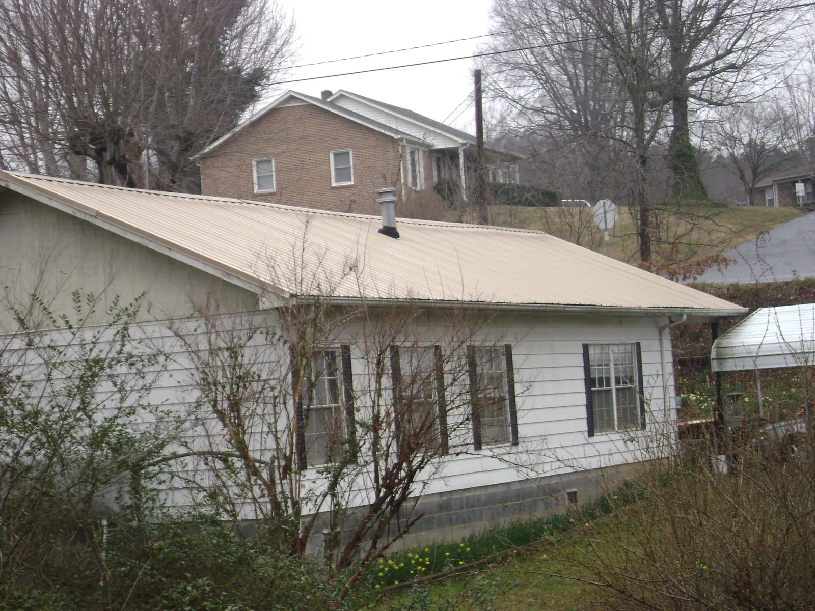Tan metal roof on a white sided house set into a hillside — Commercial Roofing by Roofing Brothers in Lenoir City